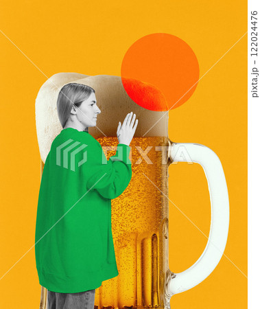Woman in green sweatshirt placing hand on giant frothy beer mug against bright yellow background with decorative orange circle. Creative art 122024476