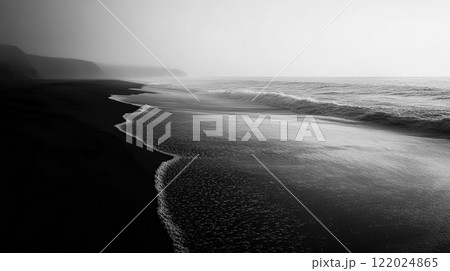 Black and white photo of a beach with a foggy sky in the background. The water is calm and the beach is empty 122024865