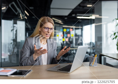 Angry female boss yelling at colleagues sitting inside office. Businesswoman on online business meeting conference, using laptop for video call. 122025705