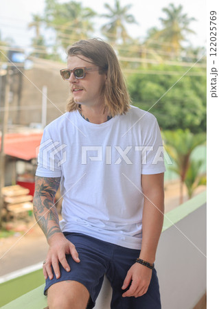 A man in sunglasses and a white tshirt stands on a balcony 122025769