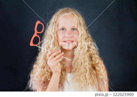 Portrait of cheerful young girl posing with photo booth props glasses on black background 122025900