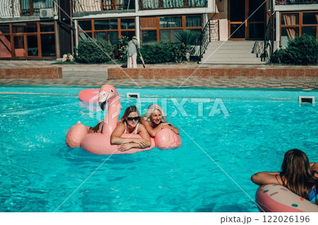 Three women are floating in the pool on inflatable floats. One of the floats is pink and has a flamingo on it. The women are smiling and enjoying their time in the water. 122026196