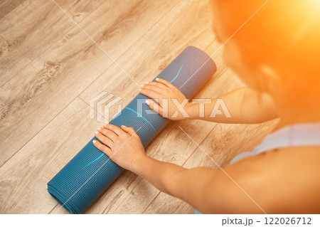Woman hands rolled up yoga mat on gym floor in yoga fitness training room. Home workout woman close up hands rolling foam yoga gym mat. Woman barefoot home workout sportive healthy lifestyle concept 122026712