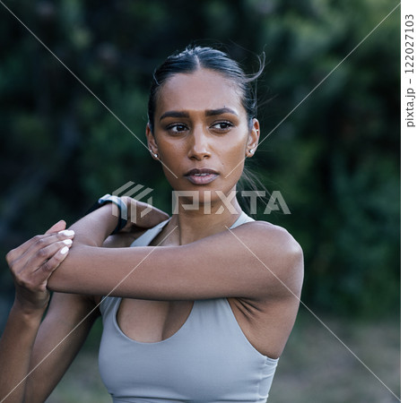 Portrait of young slim athlete warming up upper body while standing outdoors  122027103