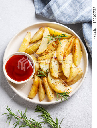Baked potato wedges with spices, fresh rosemary and tomato sauce on a plate on a light background 122027324
