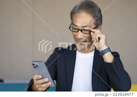 メガネをかけてスマートフォンの画面を見る60代の男性 122028477