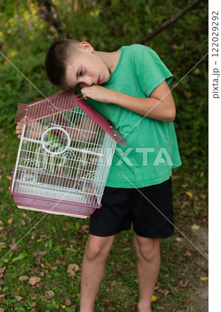 Boy sadly holds a birdcage with a small bird inside. Outdoors, nature setting. Boy sadly holds a birdcage with a small bird inside. Outdoors, nature setting. 122029292
