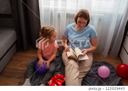 Top view of kindergarten teacher reads an educational fairy tale to a little Caucasian girl. Concept of preschool development 122029443