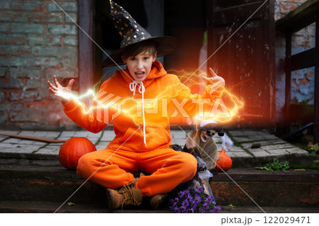 A child in an orange costume and a wizard hat for Halloween. The boy holds the skeleton and conjures a magical magical lightning bolt A child in an orange costume and a wizard hat for Halloween. The boy holds the skeleton and conjures a magical magical lightning bolt 122029471