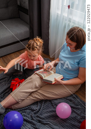 A speech therapist teaches a girl to pronounce sounds correctly. A woman and a child are reading a book together. Vertical. The concept of preschool education 122029473