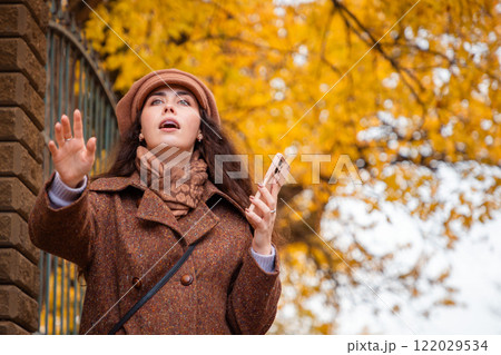 Bottom view of a Caucasian woman in a coat and hat holding a phone and waving her hand to stop a taxi. City modern lifestyle 122029534