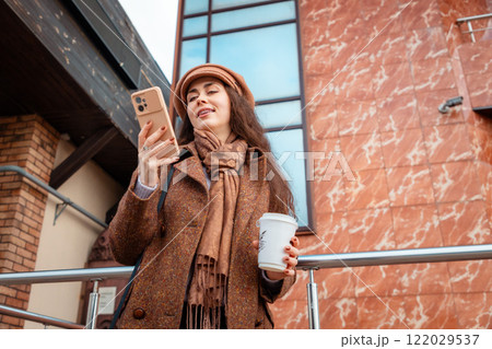 Bottom view of a young Caucasian woman smiling happily and using a smartphone. There is a modern building in the background. The concept of urban life 122029537