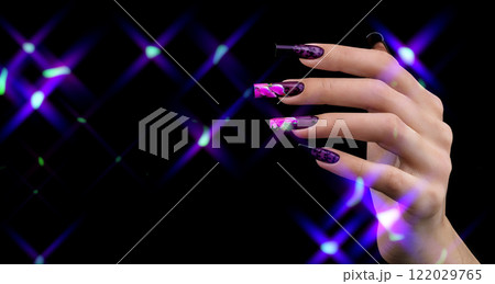 A hand with a beautiful manicure in magical light reflections on a black background. Nail design. Extended nails. A hand with a beautiful manicure in magical light reflections on a black background. Nail design. Extended nails. 122029765
