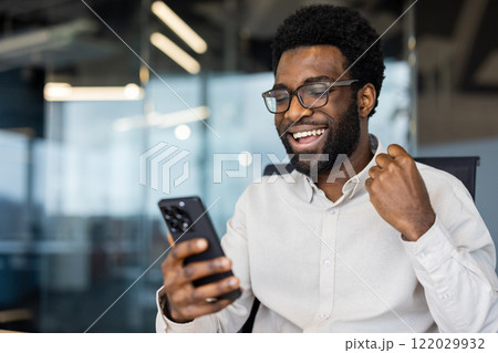 Successful man close up inside office celebrating victory and successful achievement results, businessman holding phone in hands, received notification of triumph. Successful man close up inside office celebrating victory and successful achievement results, businessman holding phone in hands, received notification of triumph. 122029932