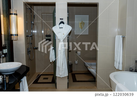 Primary bathroom interior with free standing bath tub floating cabinets walk in shower windows with black frames spa robe hanging on a hanger grey slate flooring 122030639