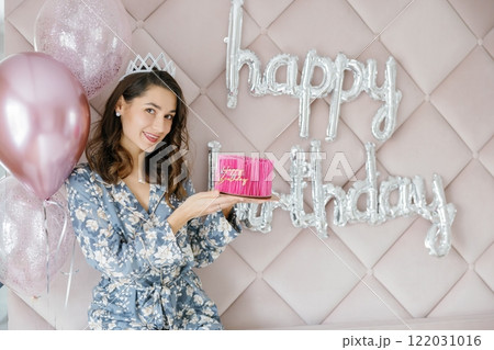 Woman celebrating birthday holding pink cake with balloons and happy birthday sign 122031016