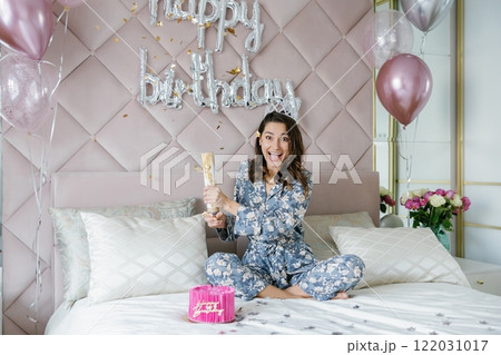 Young woman celebrating birthday opening firecracker on bed 122031017