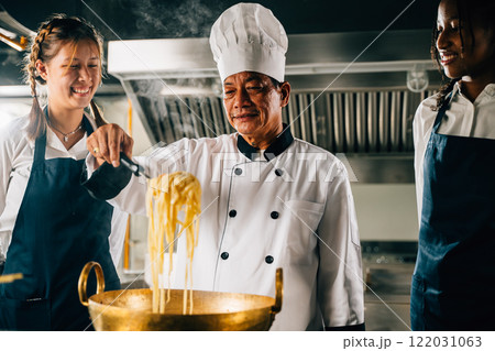 Chef in kitchen educates students. Schoolgirls in uniform make Japanese noodle. Kids at stove with teacher. Portrait of smiling students learning is modern education. 122031063