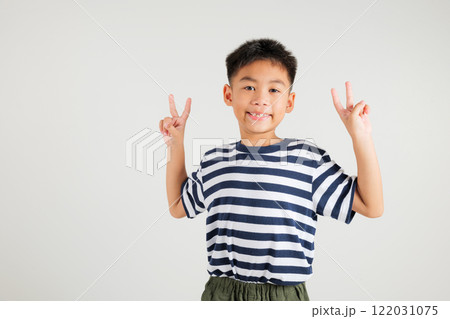 Asian young kid boy showcases optimism and peace by gesturing victory and peace signs in a studio shot with a white background. primary child joyful smile speaks of success, V sign finger 122031075