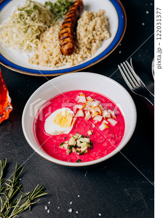 Colorful business lunch with grilled sausage, couscous, cabbage salad, and beet soup with boiled egg Colorful business lunch with grilled sausage, couscous, cabbage salad, and beet soup with boiled egg 122031377