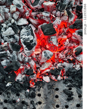 Glowing charcoal embers provide warmth and energy for outdoor cooking during an evening barbecue gathering 122031666
