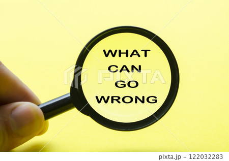 Hand holding magnifying glass with text what can go wrong. Fact finding concept. 122032283