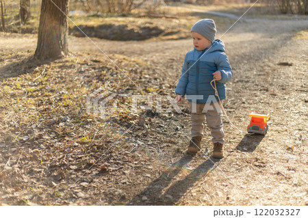 Happy baby child outdoor. Little toddler boy with toy car having fun on walk in park. Baby son smiling playing outdoor. Little child resting walking in nature. Little toddler child having fun on walk 122032327