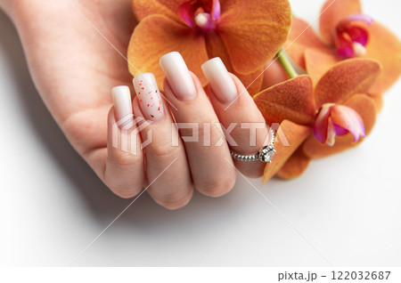 Woman hand showing stylish trendy nude manicure holding orange orchid flowers Woman hand showing stylish trendy nude manicure holding orange orchid flowers 122032687