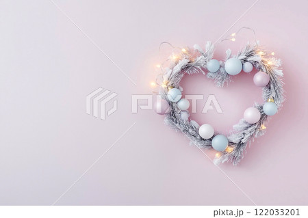 Heart-shaped holiday wreath with ornaments and fairy lights on pink background. Modern and elegant minimalist Christmas decoration Heart-shaped holiday wreath with ornaments and fairy lights on pink background. Modern and elegant minimalist Christmas decoration 122033201