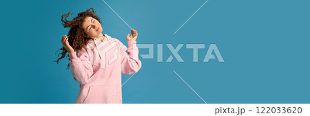 Carefree, calm young girl shaking her head of joy, hair flowing against blue studio background with negative space to insert text. 122033620