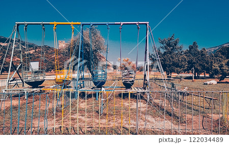 Vibrant swings in a quiet playground surrounded by green hills on a clear sunny day Vibrant swings in a quiet playground surrounded by green hills on a clear sunny day 122034489