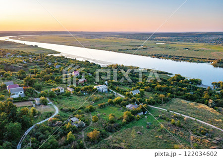 Scenic riverside landscape at sunset reveals serene village tranquility and lush greenery. Aerial photo. Scenic riverside landscape at sunset reveals serene village tranquility and lush greenery. Aerial photo. 122034602
