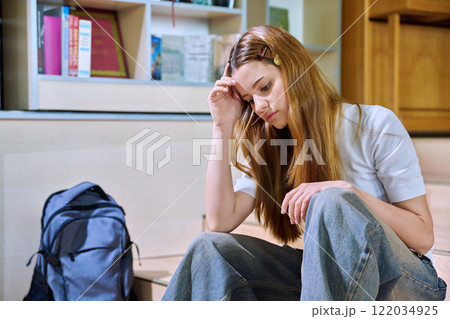 Upset sad teenage girl high school student sitting on floor in library classroom Upset sad teenage girl high school student sitting on floor in library classroom 122034925