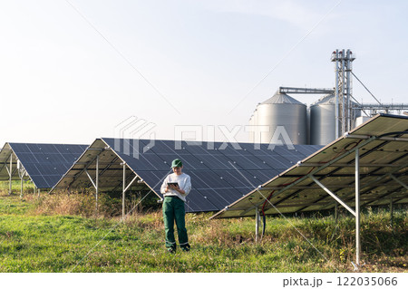 Female farmer with digital tablet on a modern farm using solar panels. Agricultural silos in the background. Female farmer with digital tablet on a modern farm using solar panels. Agricultural silos in the background. 122035066