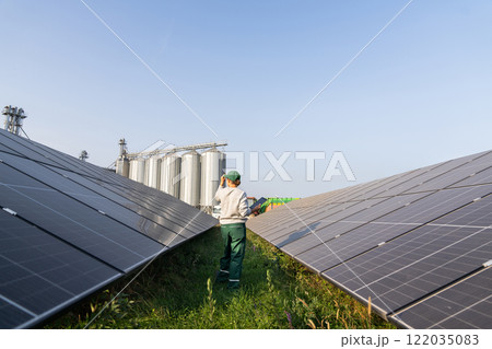 Female farmer with digital tablet on a modern farm using solar panels. Agricultural silos in the background. Female farmer with digital tablet on a modern farm using solar panels. Agricultural silos in the background. 122035083