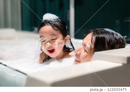 A woman and a child are in a bathtub, with the woman smiling and the child laughing. Scene is happy and playful 122035475
