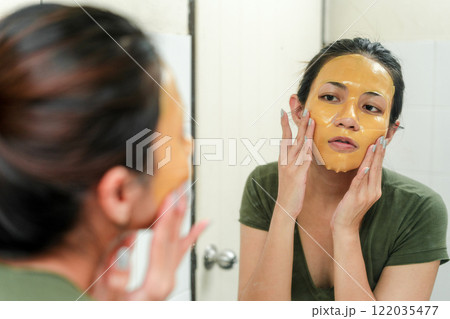 Asian Woman Applying Natural Face Mask in Bathroom Reflection for Skincare Routine and Self-Care 122035477