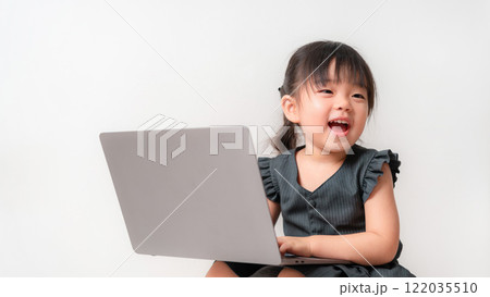 Asian girl using a laptop indoors. She is focused on the screen, pointing with her finger while sitting against a plain white background. Asian girl using a laptop indoors. She is focused on the screen, pointing with her finger while sitting against a plain white background. 122035510