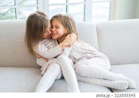 Happy family sisterly love. Two funny little twin sisters girls hugging with love care playing together at home indoors. Happy children lifestyle. Identical twin girls hugs. Girls friendship and youth 122035545