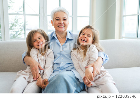 Happy family at home. Two little girls sisters twins grandmother enjoying time together. Good time at home. Grandma granddaughters child kids emotional bonding hugging together. Family generations Happy family at home. Two little girls sisters twins grandmother enjoying time together. Good time at home. Grandma granddaughters child kids emotional bonding hugging together. Family generations 122035546