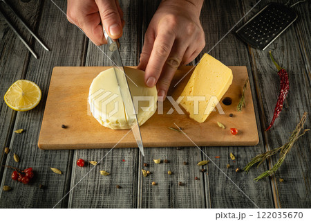 Hands expertly cut a creamy cheese while surrounded by herbs, spices, and a lemon on a weathered wooden surface. This activity captures the essence of culinary artistry and craftsmanship Hands expertly cut a creamy cheese while surrounded by herbs, spices, and a lemon on a weathered wooden surface. This activity captures the essence of culinary artistry and craftsmanship 122035670