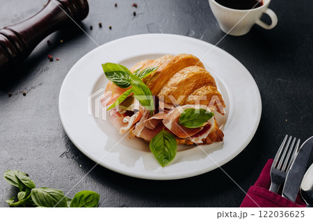 Fresh croissant sandwich with prosciutto and basil served on plate, perfect for a gourmet breakfast Fresh croissant sandwich with prosciutto and basil served on plate, perfect for a gourmet breakfast 122036625