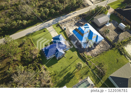Hurricane Ian damaged house rooftop covered with protective plastic tarp against rain water leaking until replacement of asphalt shingles. Aftermath of natural disaster 122036781