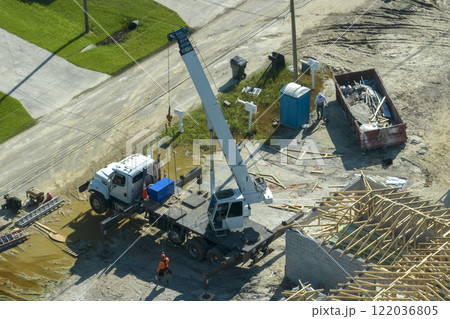 Lifting crane truck and builders working on roof construction of unfinished residential house with wooden frame structure in Florida suburban area. Housing development concept 122036805
