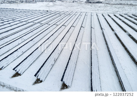 Aerial view of sustainable electrical power plant with solar photovoltaic panels covered with snow in winter for producing clean energy. Concept of low effectivity of renewable electricity in north 122037252