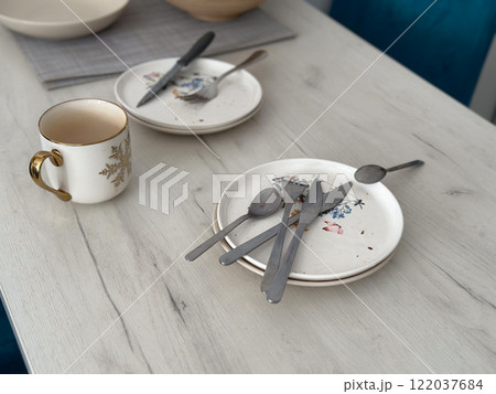 Used plates and cutlery left on a white wooden table after a meal. Messy home and dirty kitchen concept Used plates and cutlery left on a white wooden table after a meal. Messy home and dirty kitchen concept 122037684