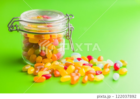 Multicolored jelly beans with various flavors in jar on green background. 122037892
