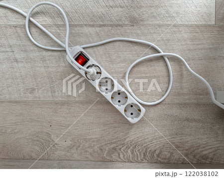 An extension cord with multiple outlets lying on a wooden floor. Practicality and utility in modern home setups. Electric power concept An extension cord with multiple outlets lying on a wooden floor. Practicality and utility in modern home setups. Electric power concept 122038102
