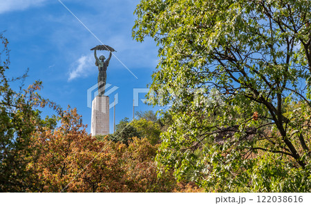 Budapest,Hungary,August 29,2022. The Statue of Liberty dominates the city from the top of the hill, it is an iconic symbol of the capital. On a beautiful summer day the treetops frame the pedestal. 122038616