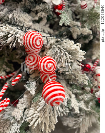 Close-up of a snow-dusted Christmas tree decorated with striped red and white ornaments. Baubles and candy canes and ribbons highlight the festive holiday atmosphere Close-up of a snow-dusted Christmas tree decorated with striped red and white ornaments. Baubles and candy canes and ribbons highlight the festive holiday atmosphere 122038640